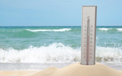 Image of Thermometer in sand near sea showing temperature, summer weather