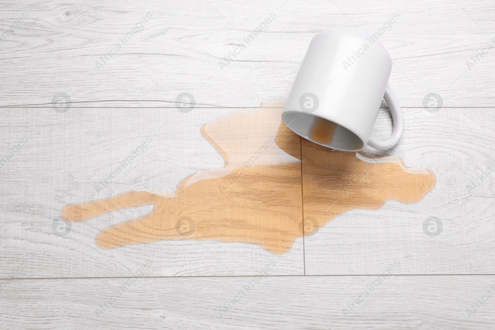 Photo of White mug with spilled liquid on wooden floor, top view