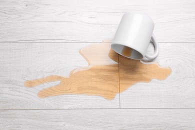 White mug with spilled liquid on wooden floor, top view