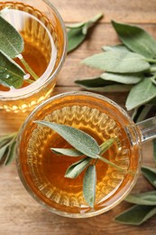 Photo of Cups of aromatic sage tea and fresh leaves on wooden table, flat lay