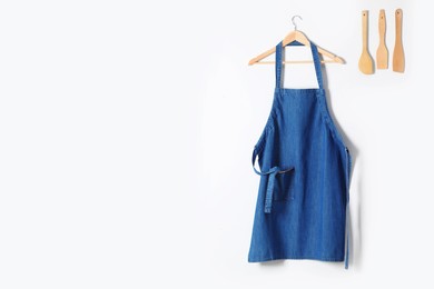 Denim apron and kitchen tools on light wall. Space for text