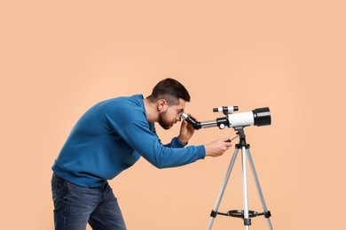 Astronomer looking at stars through telescope on beige background