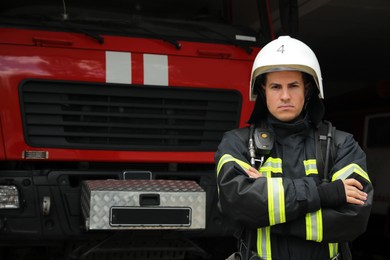 Photo of Portrait of firefighter in uniform and helmet near fire truck at station, space for text