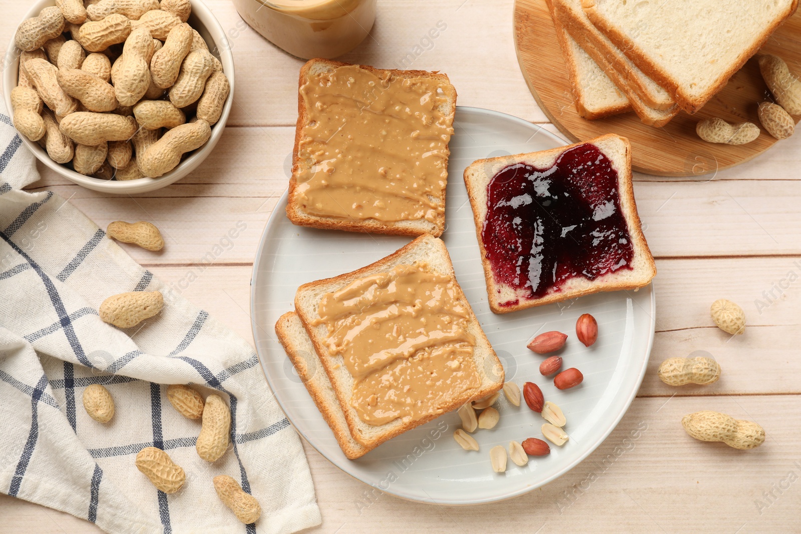 Photo of Delicious toasts with peanut butter, jam and nuts on light wooden table, flat lay