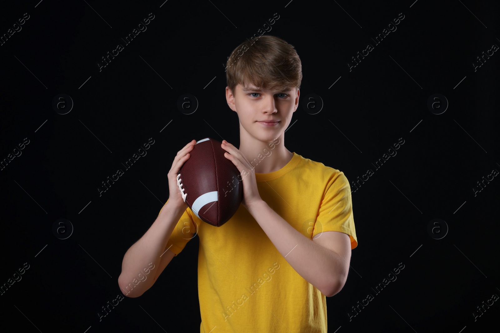 Photo of Teenage boy with american football ball on black background