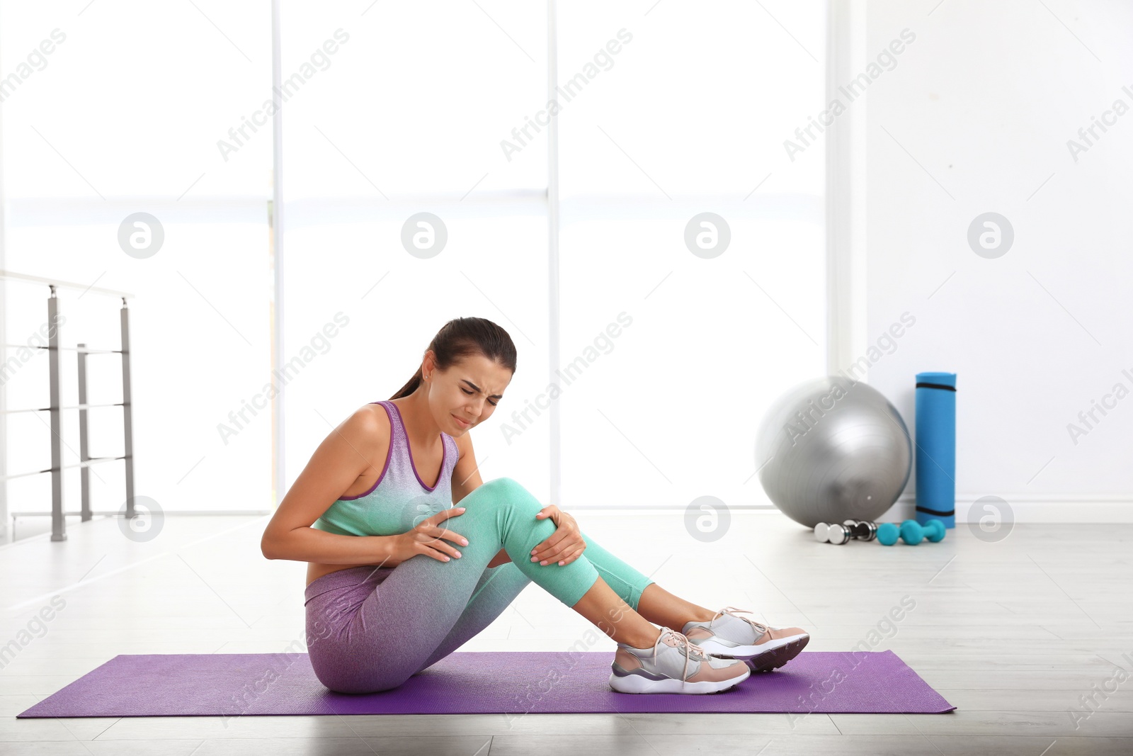 Photo of Young woman in sportswear having knee problems at gym. Space for text