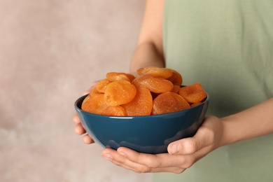 Photo of Woman holding bowl with dried apricots on color background, space for text. Healthy fruit