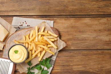 Photo of Delicious French fries and cheese sauce with parsley on wooden table, flat lay. Space for text