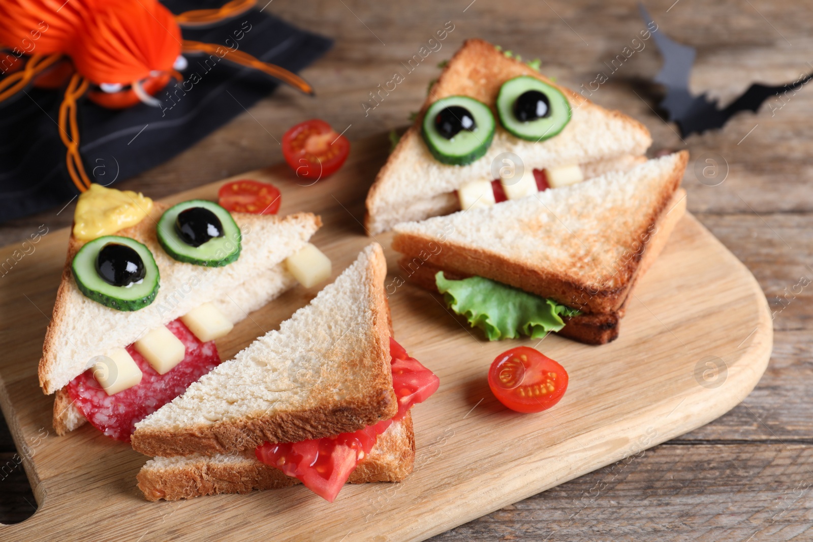 Photo of Cute monster sandwiches served on wooden board, closeup. Halloween party food