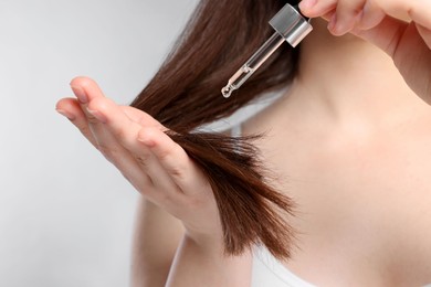 Photo of Woman applying essential oil onto hair on light grey background, closeup