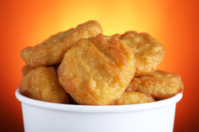 Photo of Bucket with delicious chicken nuggets on orange background, closeup