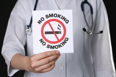 Photo of Doctor holding card with no smoking sign on black background, closeup