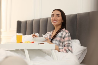 Happy young woman having breakfast on bed at home