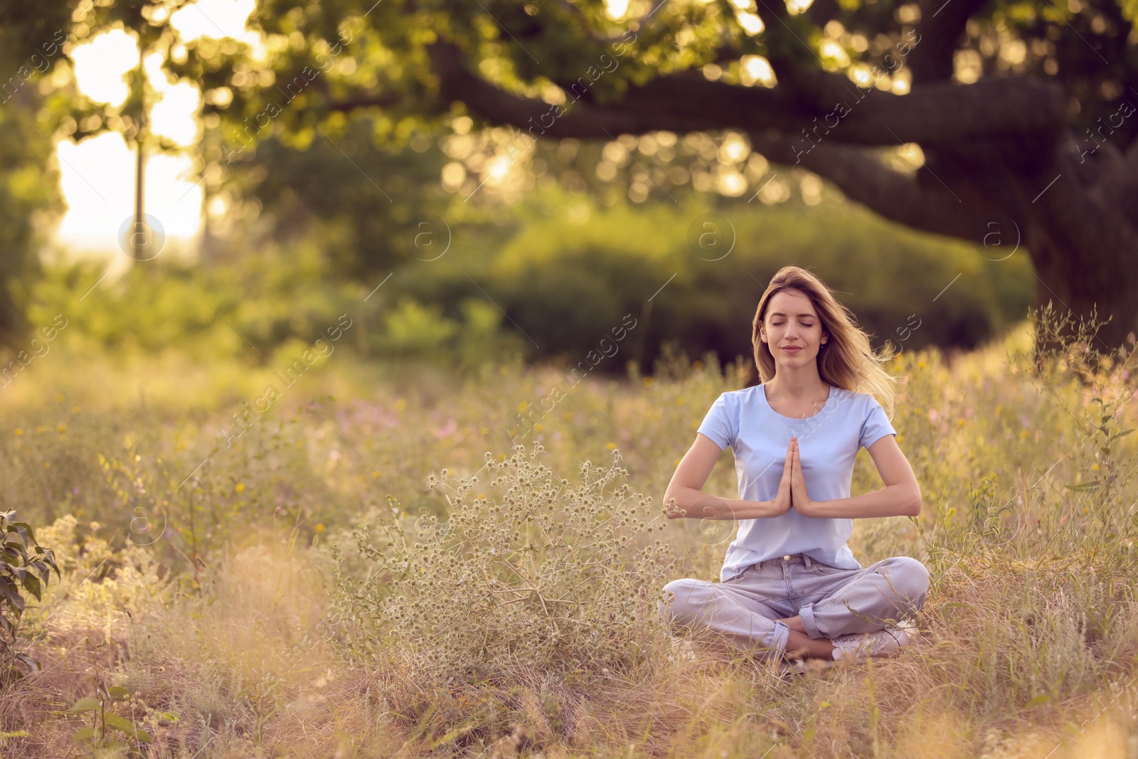 Photo of Young woman meditating on green grass in park, space for text