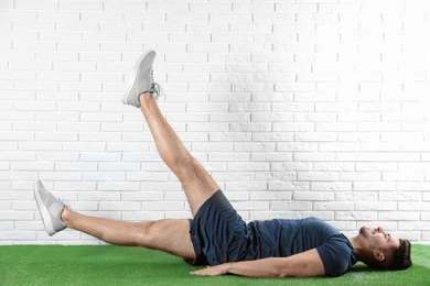 Handsome young man in sportswear doing scissors exercise on artificial green lawn near brick wall