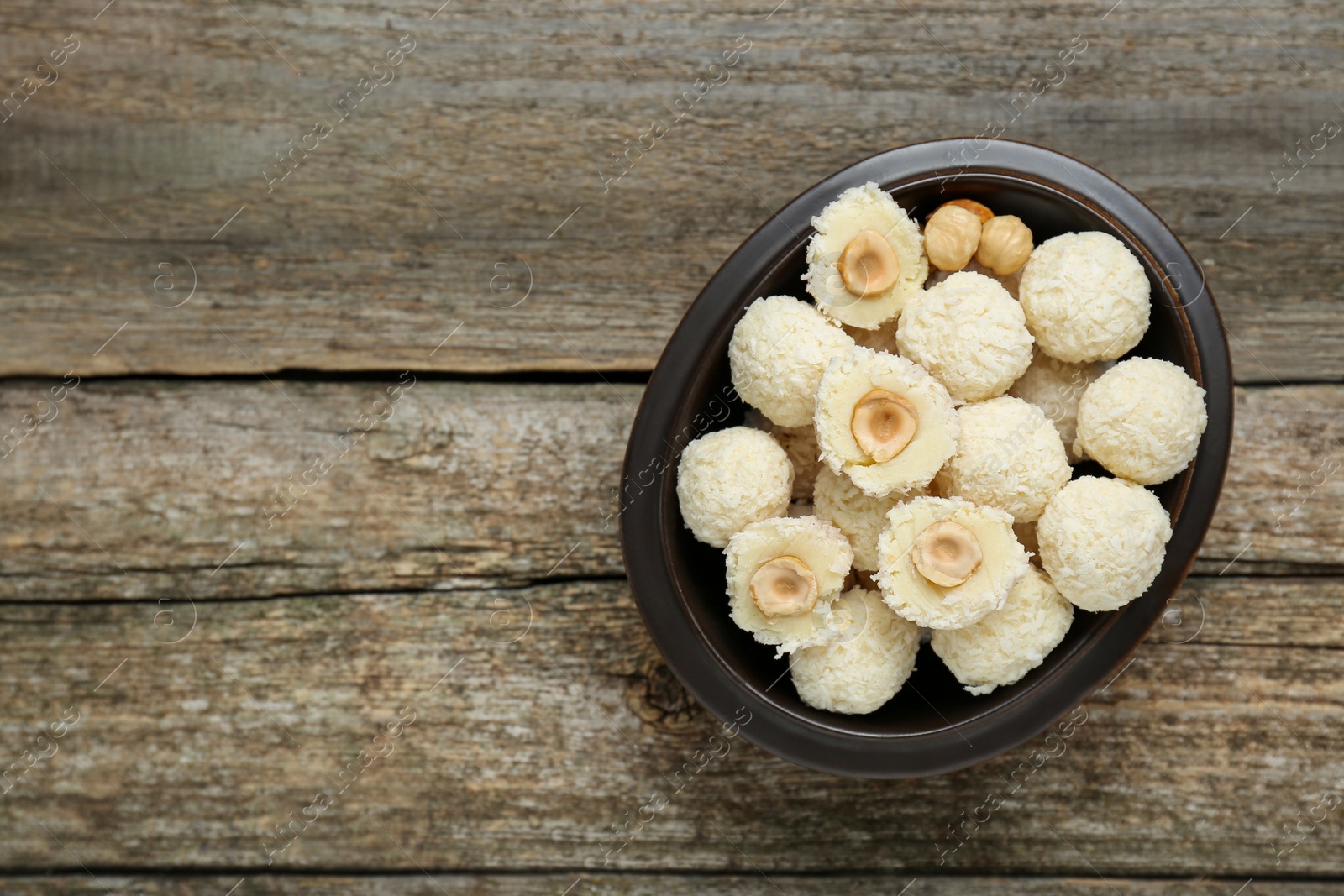 Photo of Delicious candies with coconut flakes and hazelnut on wooden table, top view. Space for text