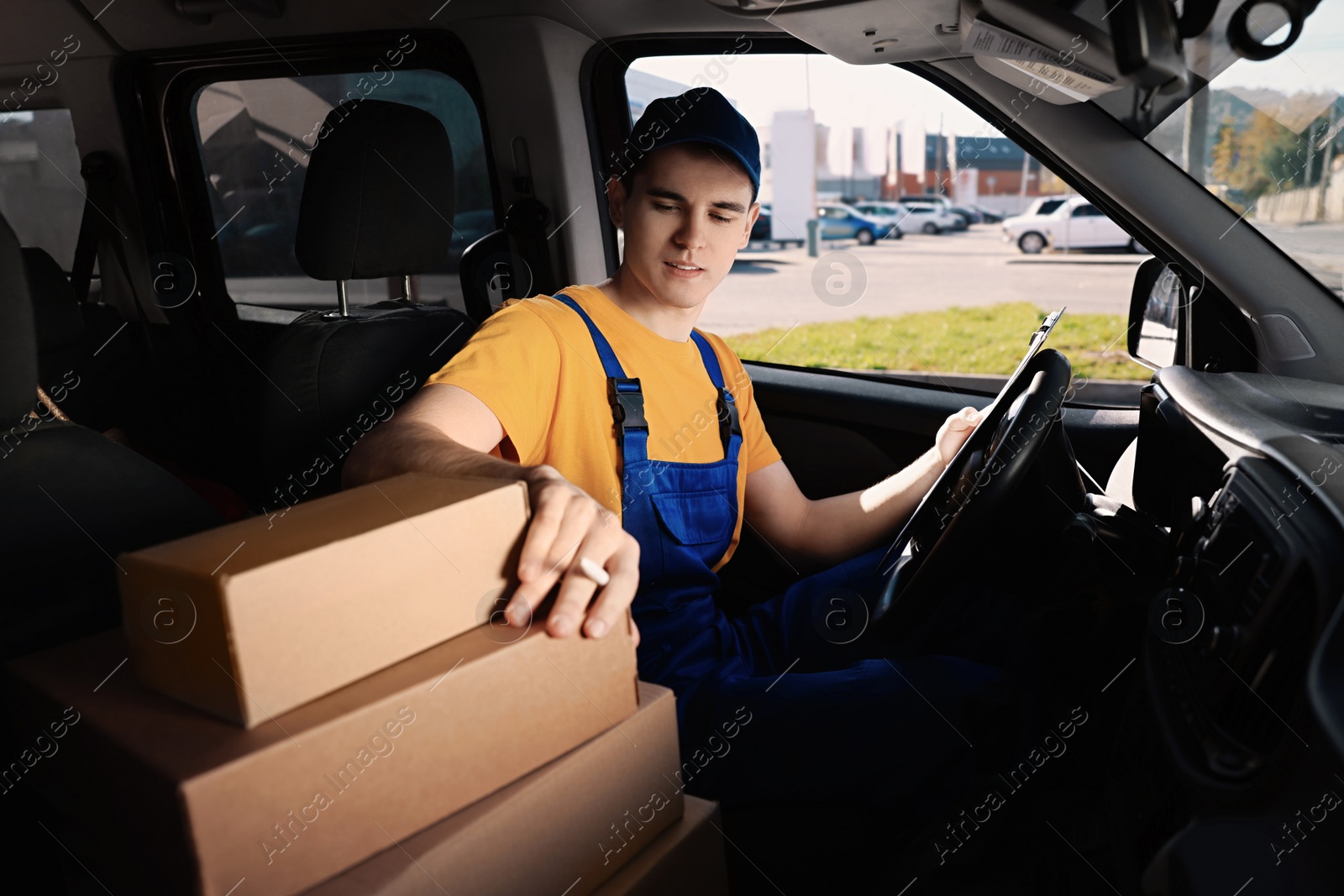 Photo of Courier with clipboard checking packages in car