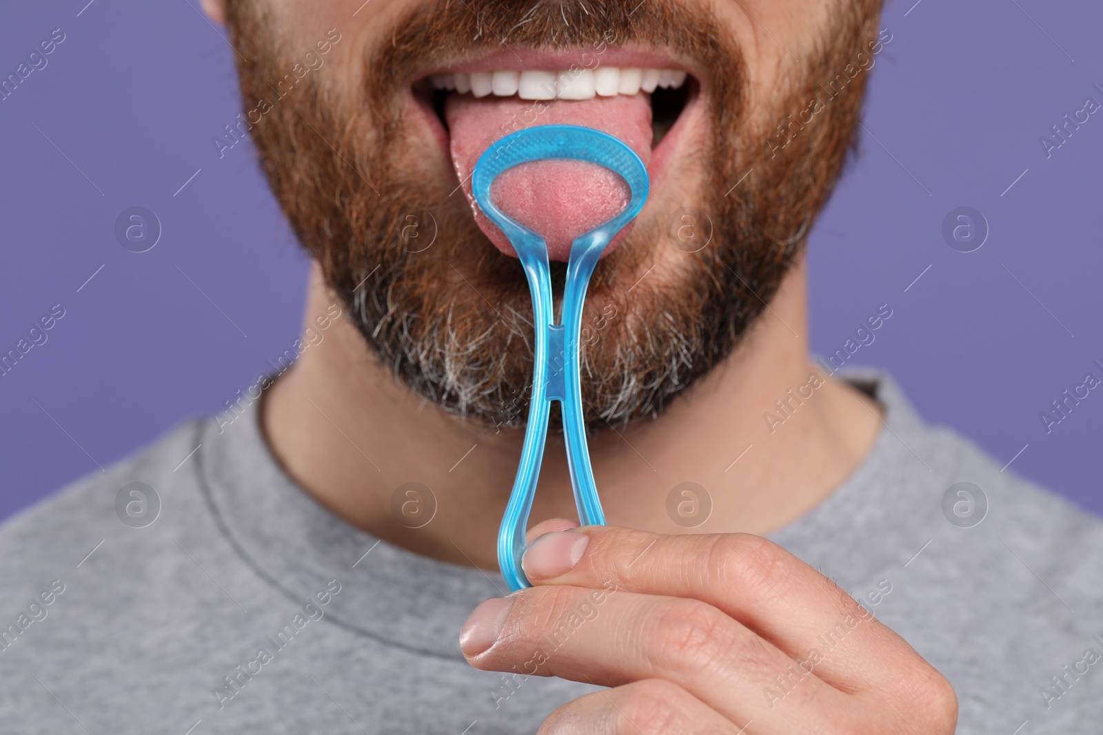Photo of Man brushing his tongue with cleaner on violet background, closeup
