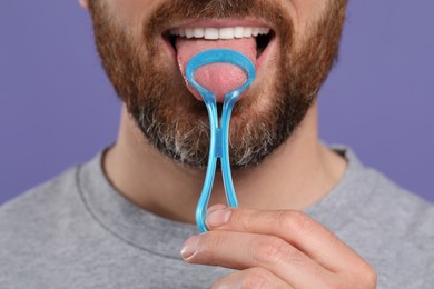 Man brushing his tongue with cleaner on violet background, closeup