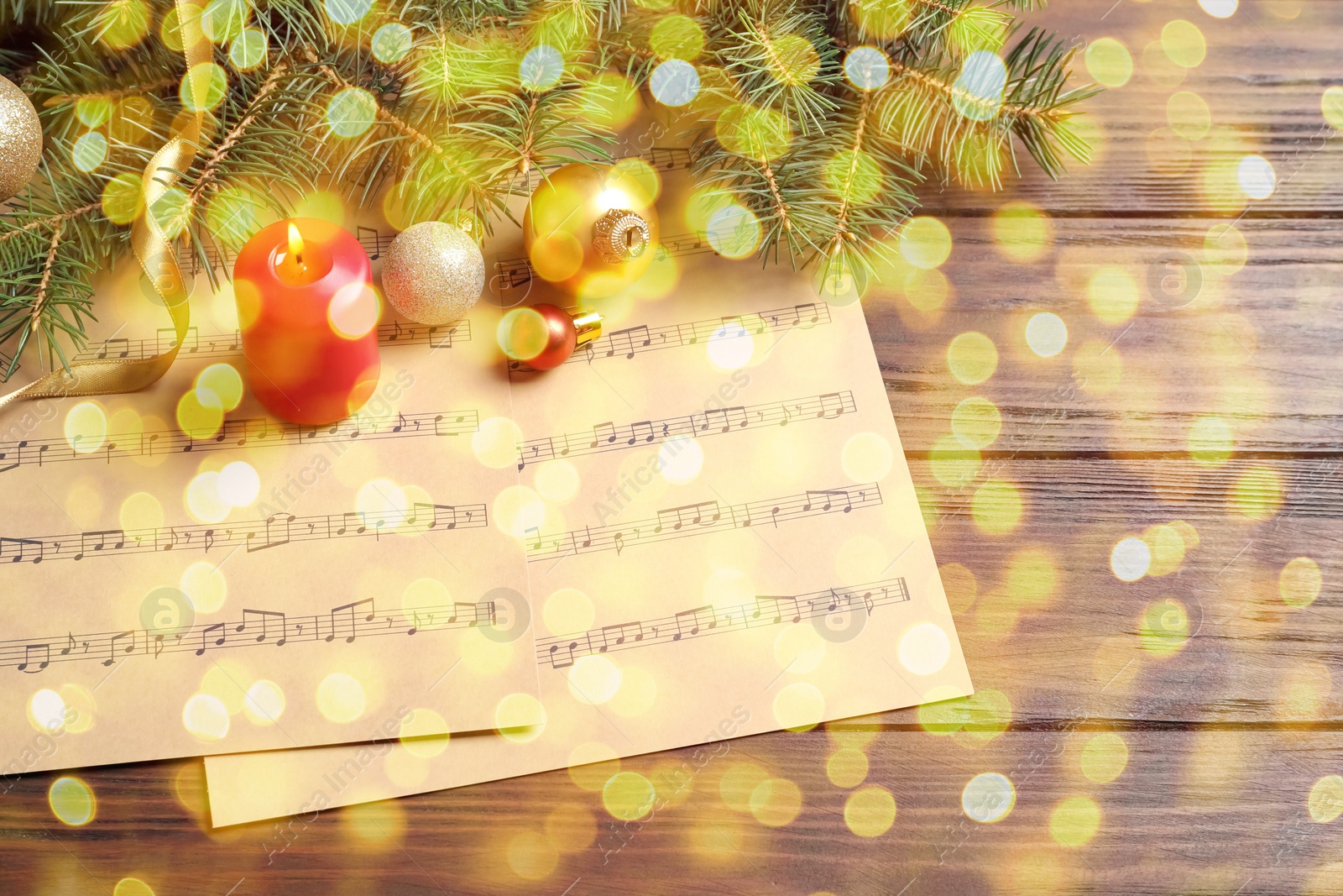 Image of Christmas and New Year music. Fir tree branch, festive decor and music sheets on wooden background, bokeh effect