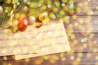 Christmas and New Year music. Fir tree branch, festive decor and music sheets on wooden background, bokeh effect