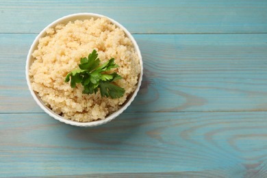 Photo of Tasty quinoa porridge with parsley in bowl on light blue wooden table, top view. Space for text