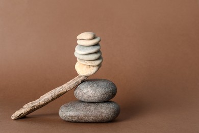 Photo of Stack of stones balancing on wooden stick against brown background, space for text. Harmony concept