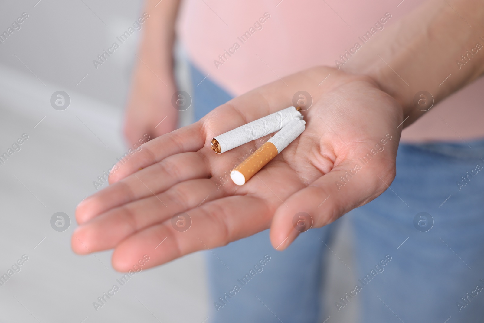 Photo of Woman holding broken cigarette on light background, closeup. Quitting smoking concept