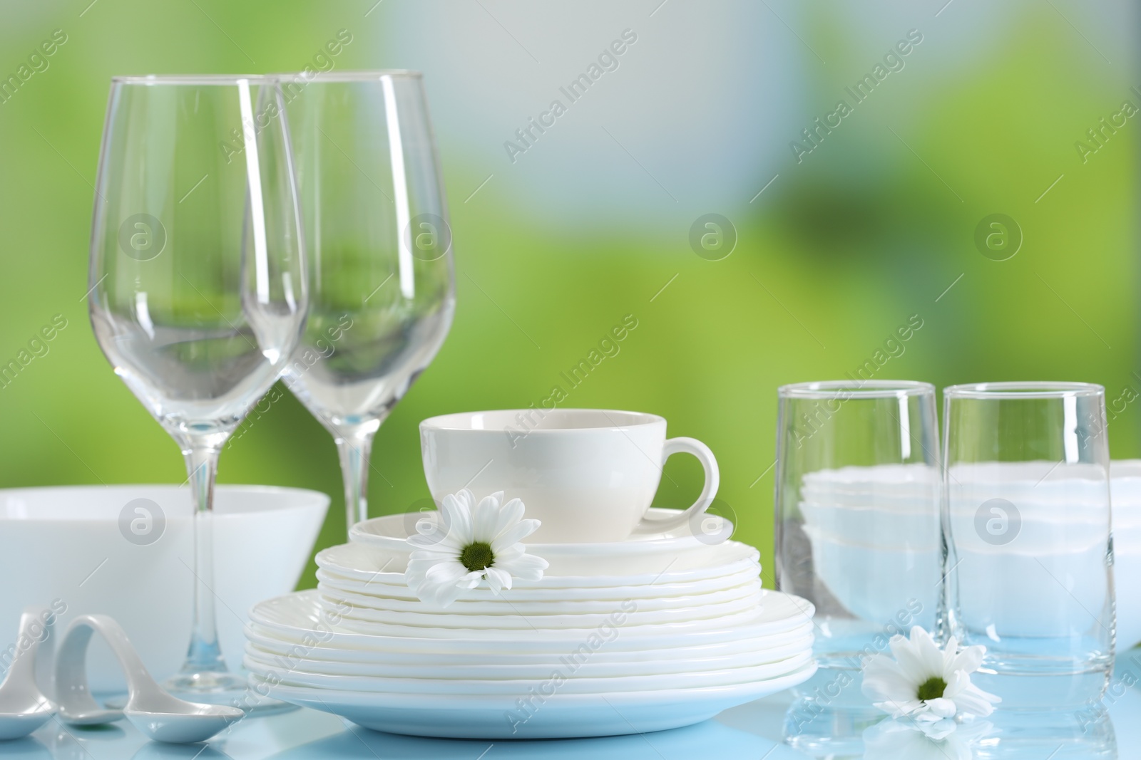 Photo of Set of many clean dishware and glasses on light blue table against blurred green background