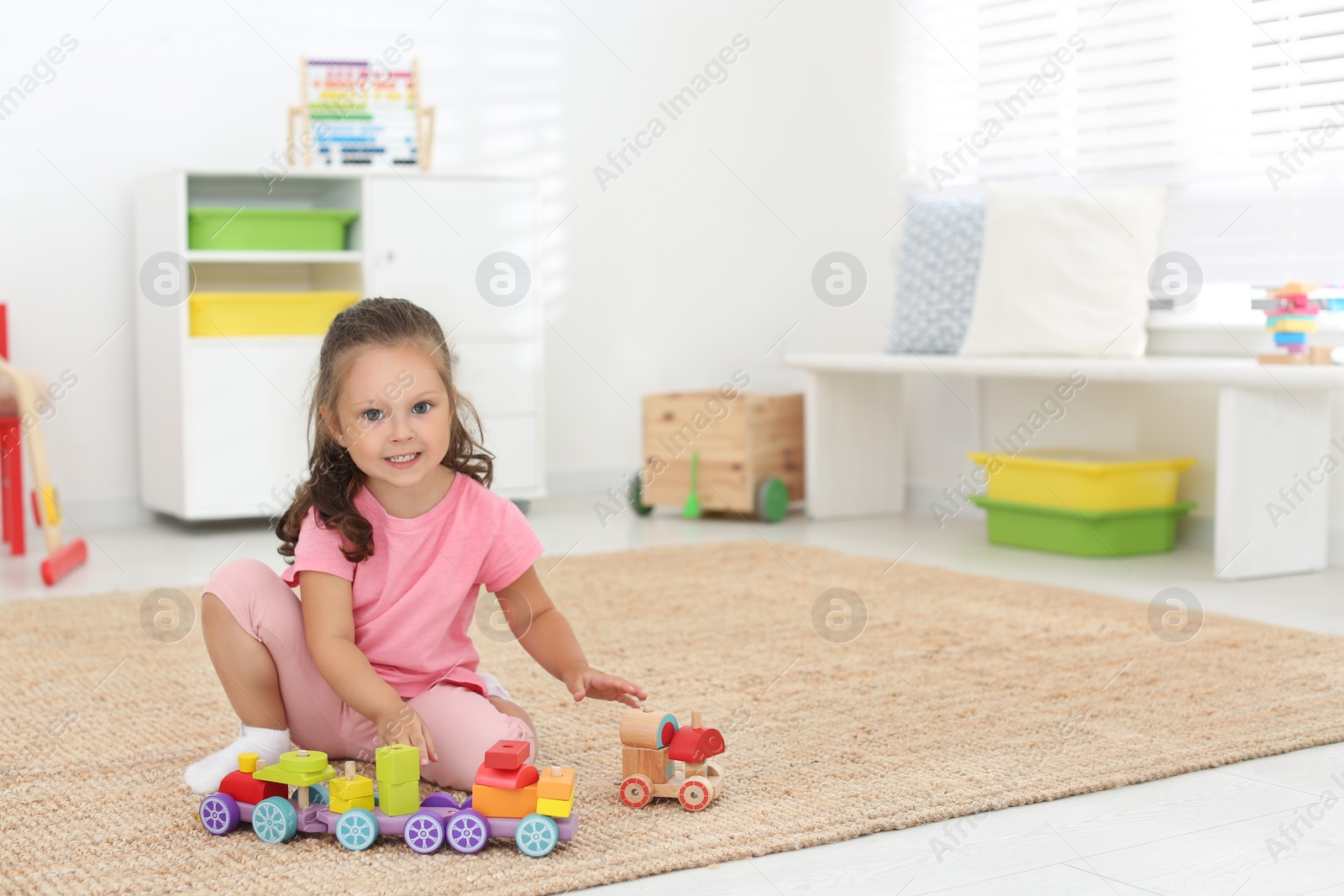 Photo of Cute little girl playing with toys on floor at home, space for text