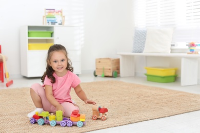 Photo of Cute little girl playing with toys on floor at home, space for text