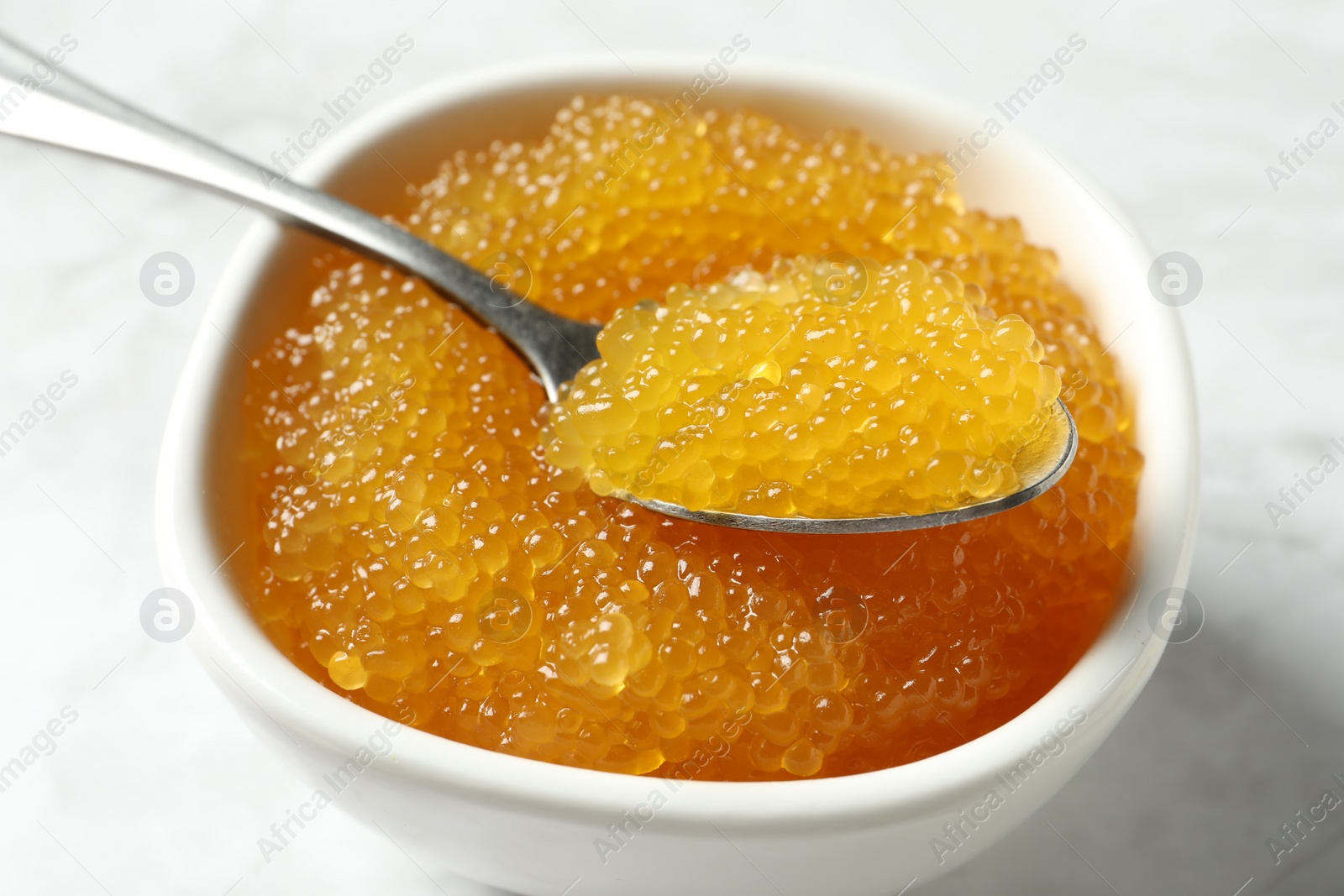 Photo of Fresh pike caviar in bowl and spoon on white table, closeup