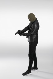 Photo of Man wearing knitted balaclava with gun on light grey background