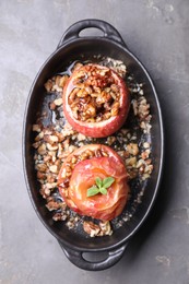 Photo of Tasty baked apples with nuts, honey and mint in baking dish on gray textured table, top view