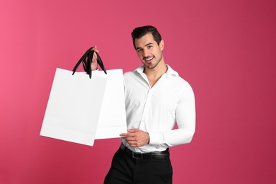 Photo of Young handsome man holding white paper bags on pink background. Mockup for design