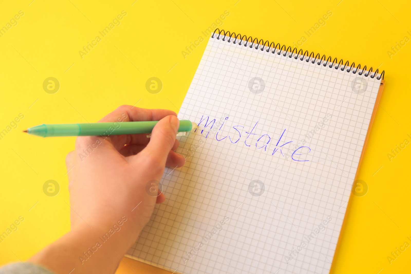 Photo of Woman erasing word Mistake written with erasable pen in notepad on yellow background, above view