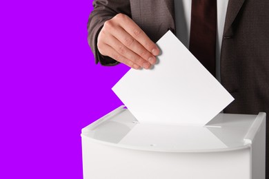 Man putting his vote into ballot box on violet background, closeup