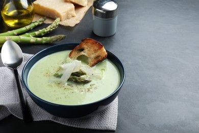 Photo of Bowl of delicious asparagus soup served on dark table, space for text