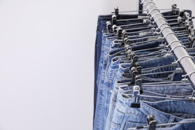 Photo of Rack with different jeans on light background, closeup. Space for text