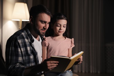 Photo of Little girl with father reading fairy tale at home in evening