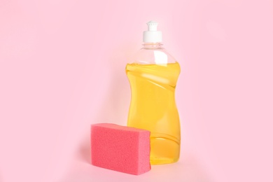 Bottle of detergent and sponge on pink background