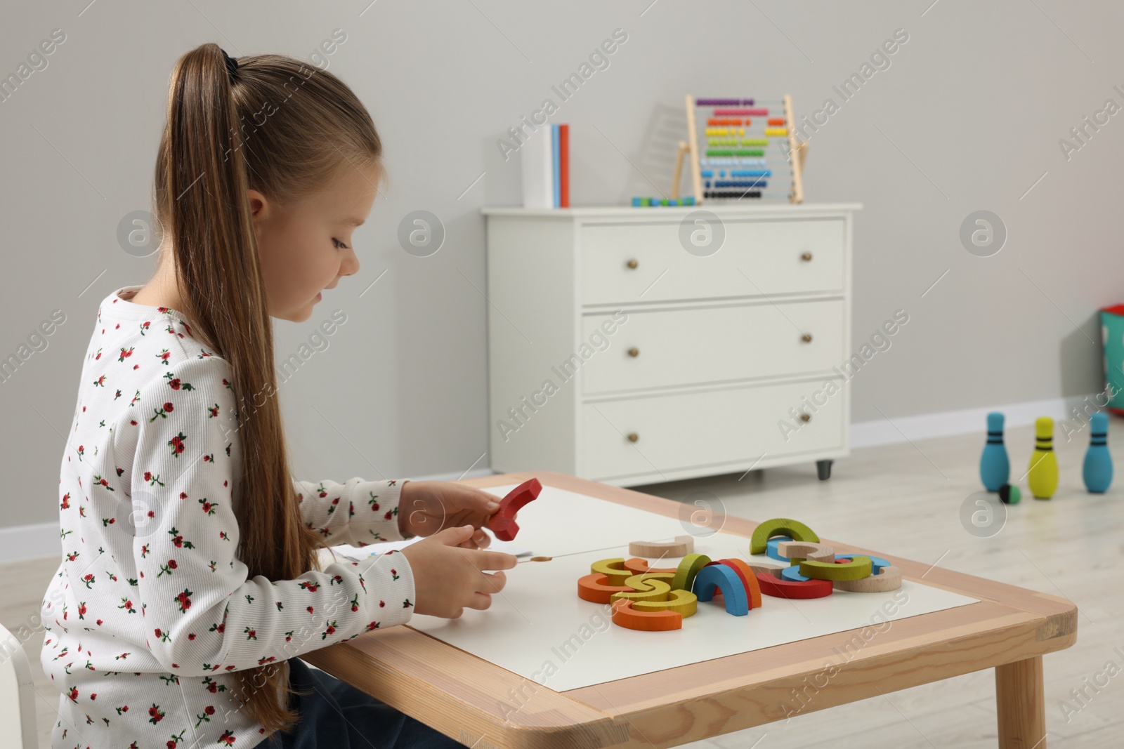 Photo of Motor skills development. Girl playing with colorful wooden arcs at white table in kindergarten