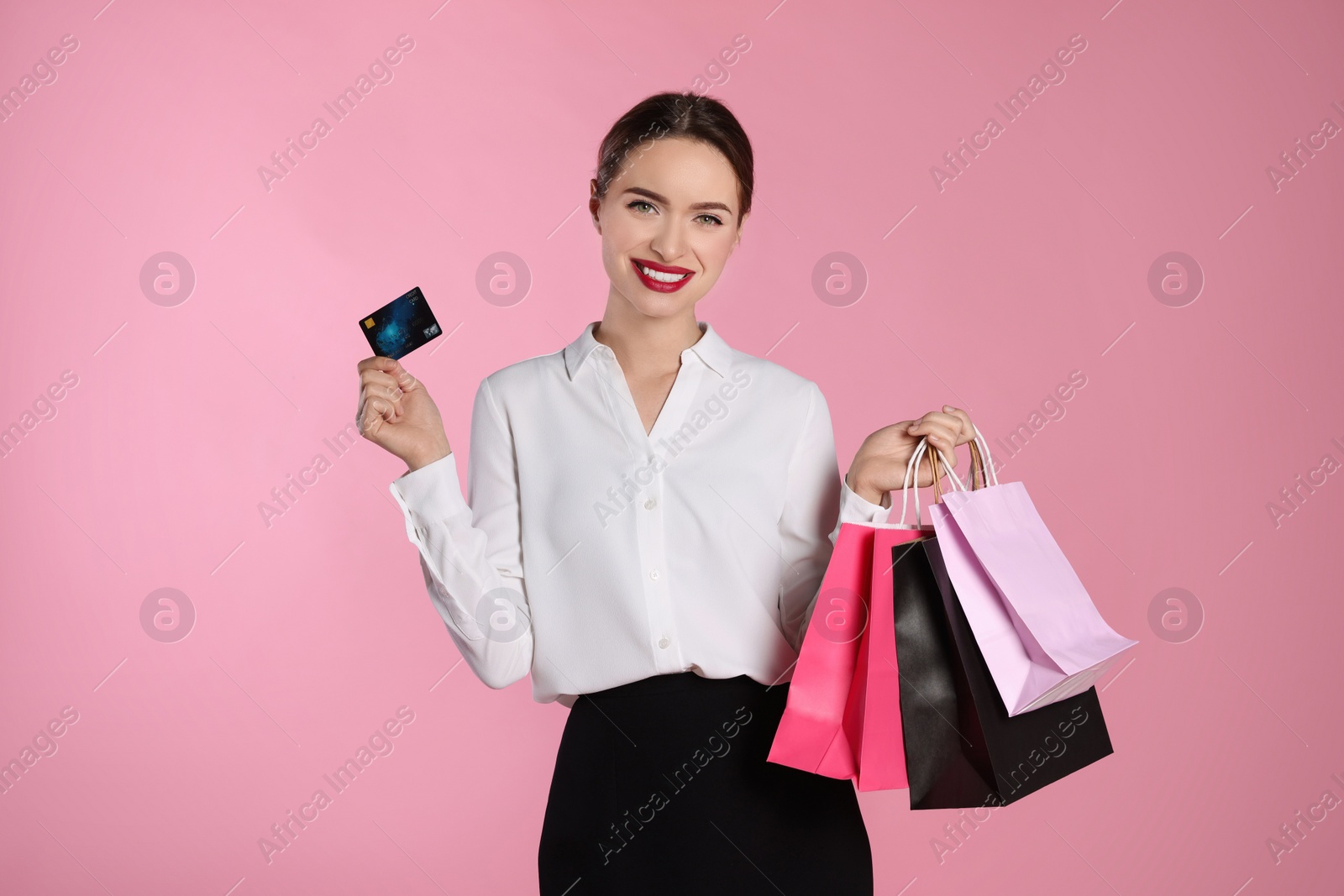 Photo of Happy young woman with shopping bags and credit card on light pink background. Big sale