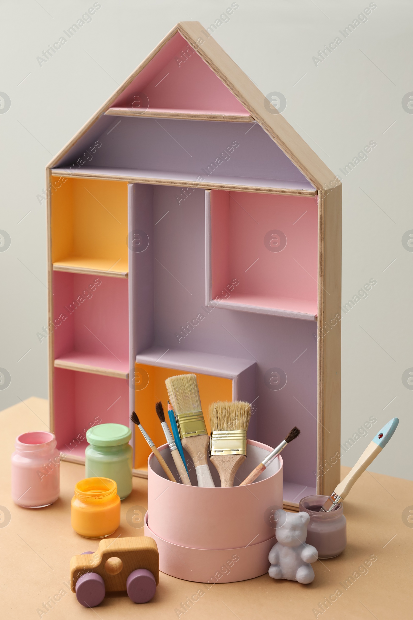 Photo of Composition with house shaped shelf and jars of paints on table. Interior element