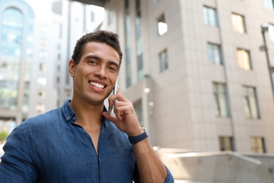 Photo of Portrait of handsome young African-American man talking on mobile phone outdoors. Space for text