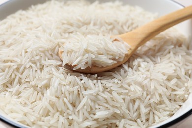 Photo of Raw basmati rice with wooden spoon in bowl, closeup