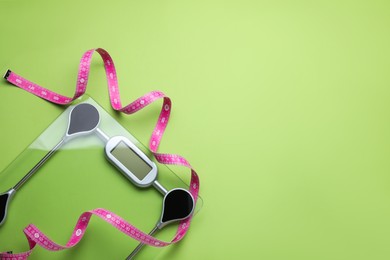 Photo of Electronic scales and measuring tape on green background, flat lay. Space for text