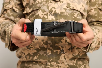 Photo of Soldier in military uniform holding medical tourniquet on light grey background, closeup
