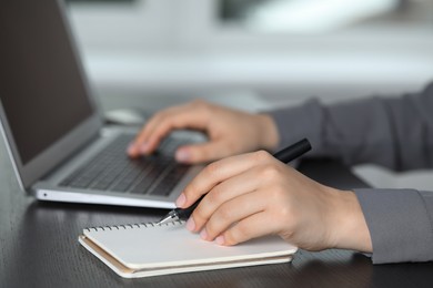 Woman with pen, laptop and notebook at wooden table, closeup. Electronic document management