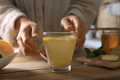 Photo of Woman making aromatic ginger tea at wooden table indoors, closeup
